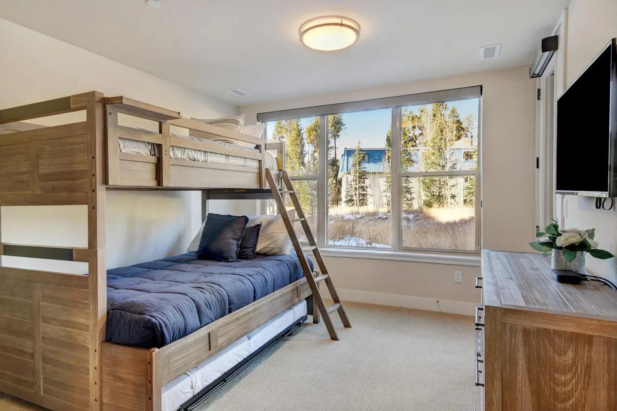 A cozy bunk room with a twin-over-full bunk bed, a large window allowing sunlight in, a wooden dresser, and a TV—perfect for sleepovers and family stays. The soft bedding and relaxed decor create a welcoming space for younger guests or friends.