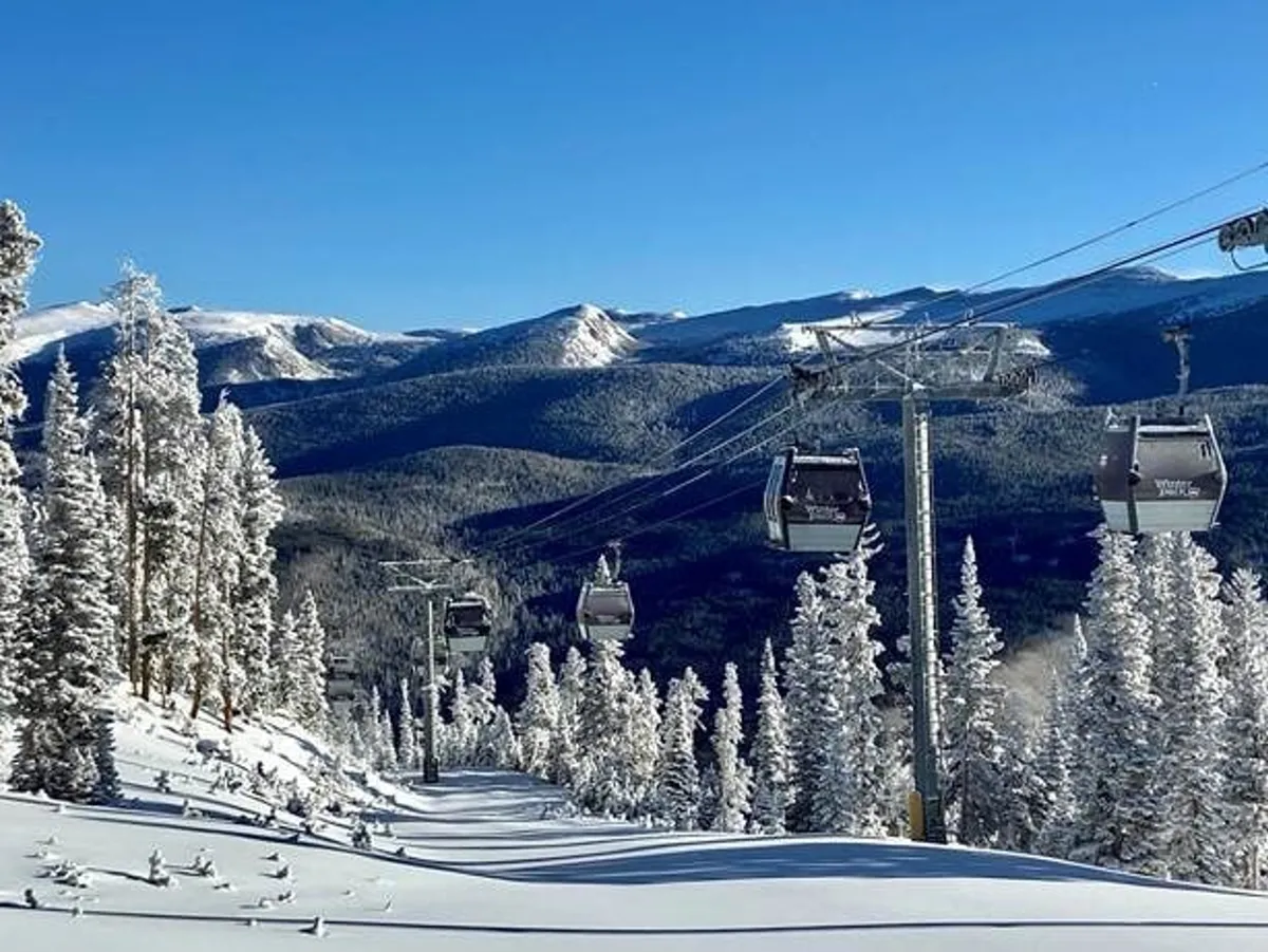 A picturesque winter scene captures ski lift gondolas gliding above snow-covered trees, with majestic mountain peaks forming a stunning backdrop. The crisp, white landscape and the presence of the lift evoke the thrill and accessibility of nearby Winter Park Resort, emphasizing winter adventure.