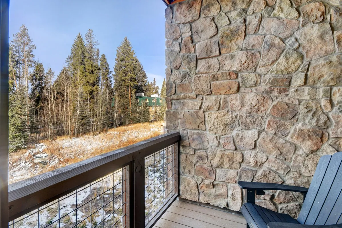 A peaceful outdoor setting with a stone wall, wooden balcony railing, and sweeping views of the natural Rocky Mountain landscape. The area invites relaxation, reading, or simply enjoying nature's tranquility from the comfort of the villa.