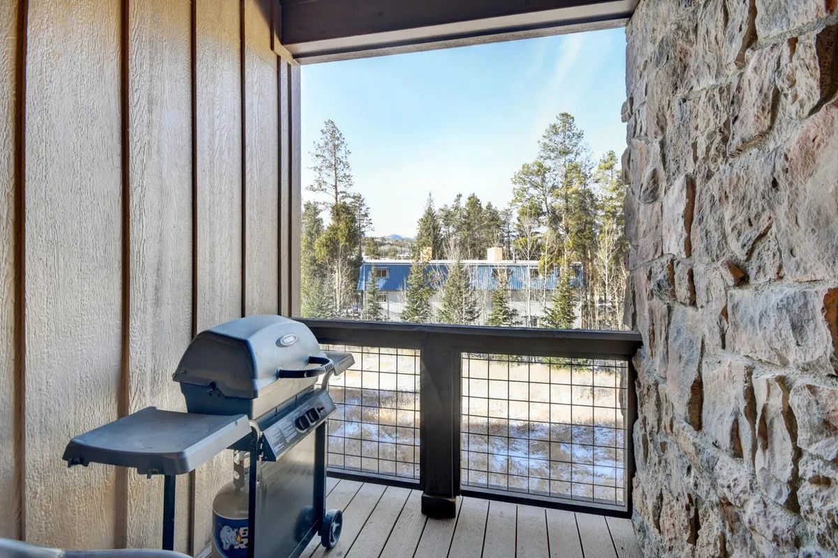 An outdoor deck with a grill, wooden railing, and panoramic views of trees and mountains. The space invites relaxation and socializing, providing a seamless connection from the home's heart to the stunning natural surroundings just beyond the glass doors.
