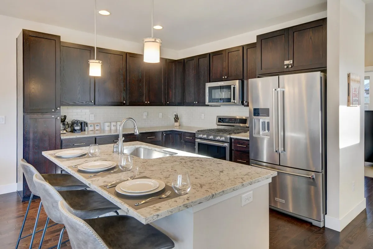 A warm, inviting kitchen and dining setup with an island countertop, stainless steel appliances, rich wood cabinetry, and a dining table set for a meal. The layout encourages both cooking and socializing, with a cozy ambiance that invites guests to share stories or enjoy a feast.