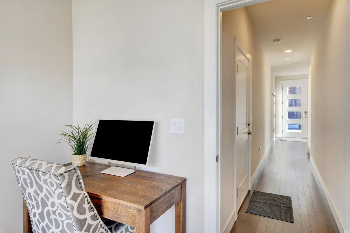 A quiet, productive workspace featuring a desk with a computer, a decorative plant, and a hallway entrance. The area is uncluttered, well-lit, and designed for comfortable focus, embodying the ideal setup for remote work or digital nomads.