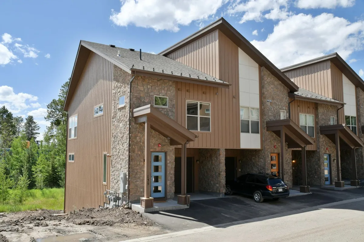 This image shows the exterior of the luxury villa, featuring a stone facade, wooden accents, large windows, and a blue front door. The inviting porch and architectural details convey a sense of comfort and high-end finishes.