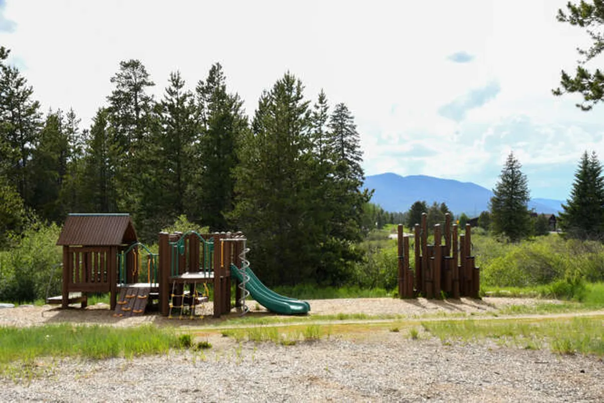 An inviting outdoor playground featuring slides and climbing structures, surrounded by a scenic natural backdrop. Children play on the equipment while families gather nearby, showcasing opportunities for outdoor recreation and community bonding.